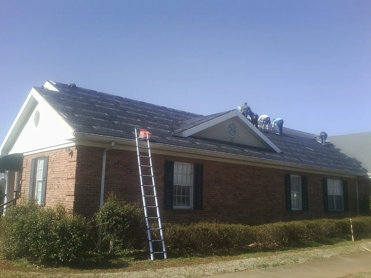 Crew tearing shingles off a brick ranch roof with a ladder set — Metal Roof Repair work by our crew in Fontana