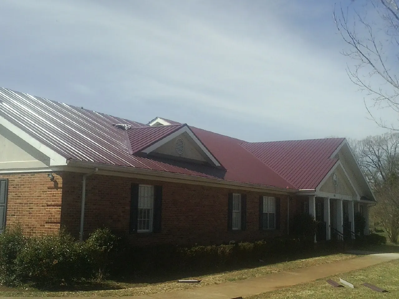 Red metal roof with gabled entries on a long brick building, from a Hail Damage Roof Repair job in Fontana